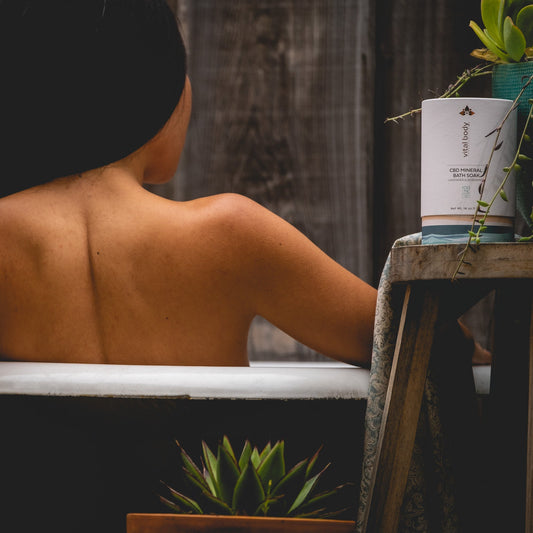 Person sitting in a bathtub with a bottle of body wash and plants around