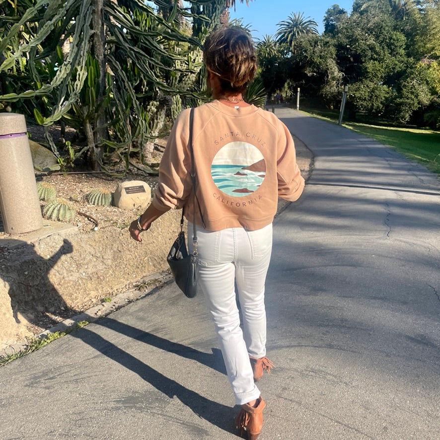 Person walking on a path wearing a beige sweatshirt with a graphic design.
