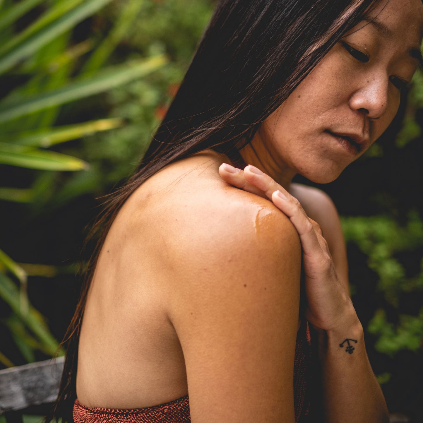 Woman with a tattoo on her arm touching her shoulder outdoors