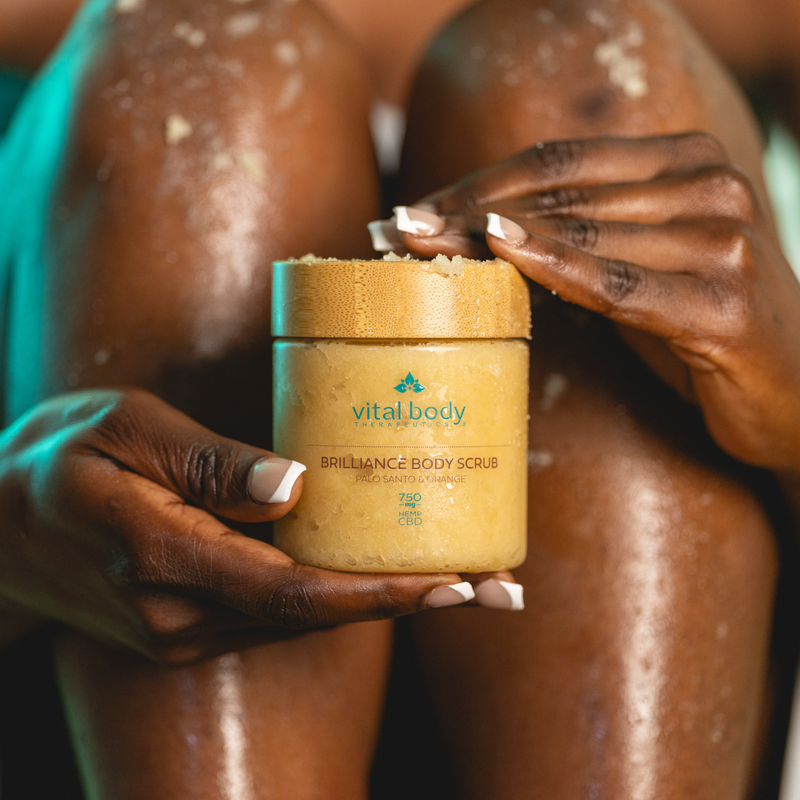 Person holding a jar of 'Vital Body' body scrub with a blurred background