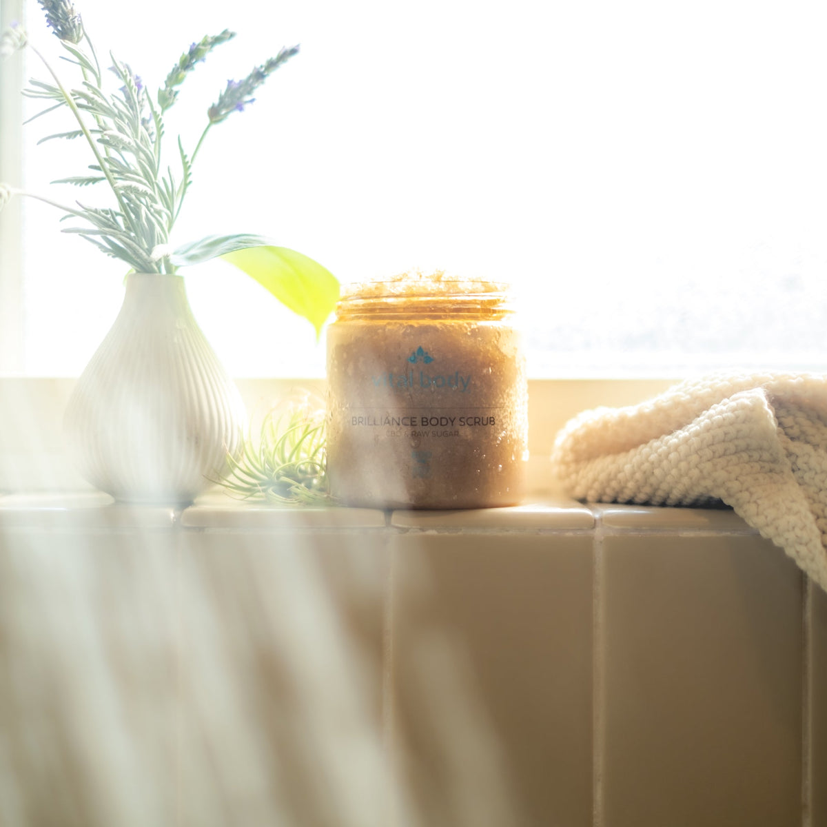 Jar of body scrub on a windowsill with plants and a towel