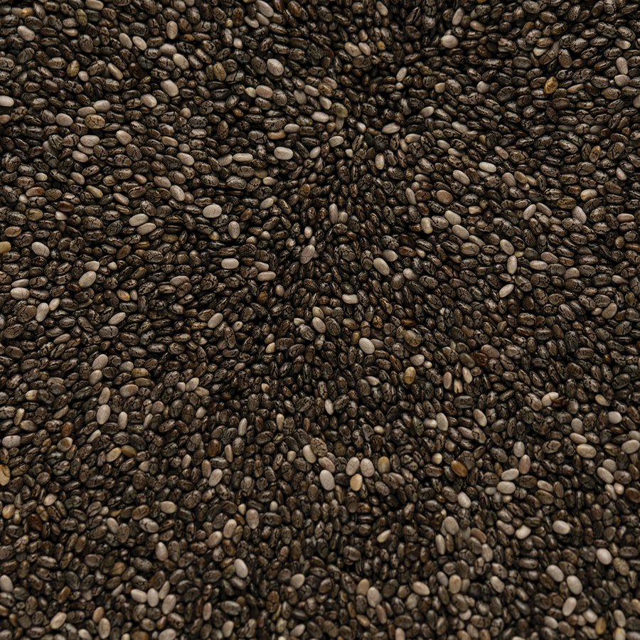 Close-up of raw chia seeds, showing small oval shapes, speckled gray and black colors, with a smooth and slightly shiny texture.