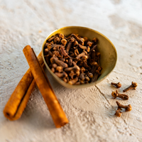 Bowl of cloves with cinnamon sticks on a textured surface