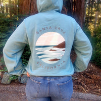 Person wearing a light blue hoodie with 'Santa Cruz California' design in a forest setting