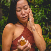 Woman applying a skincare product outdoors with greenery in the background
