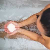 Person holding a salt crystal over a bathtub filled with water