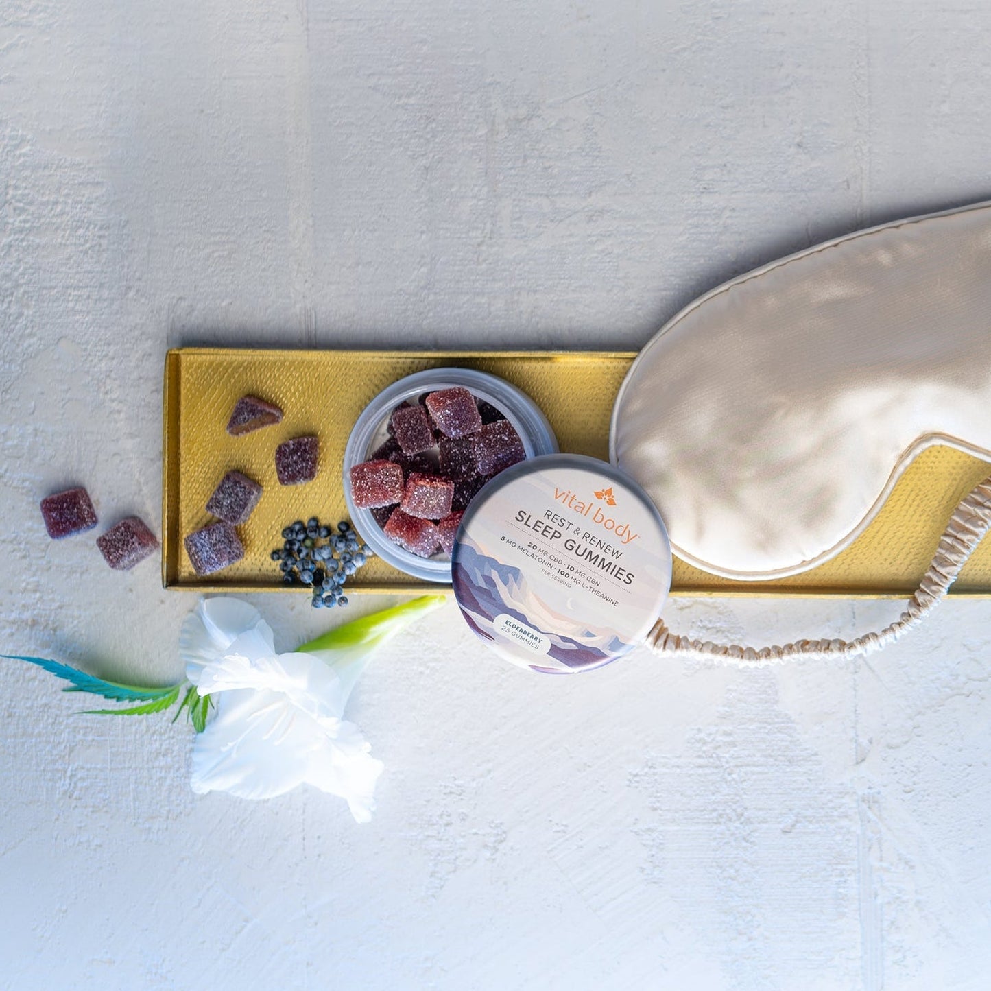 Sleep aid products including gummies, a container of gummies, and a sleep mask on a light surface.