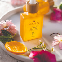 Vital Body Luminous Facial Oil bottle on a white plate with flowers and an orange slice.