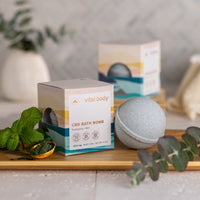 CBD bath bomb with packaging on a wooden tray with plants
