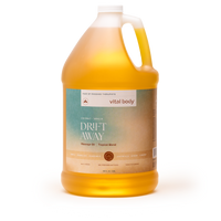 A large plastic jug of vital body Drift Away Manage Oil Tropical Blend, filled with golden yellow oil, on a clean white background.