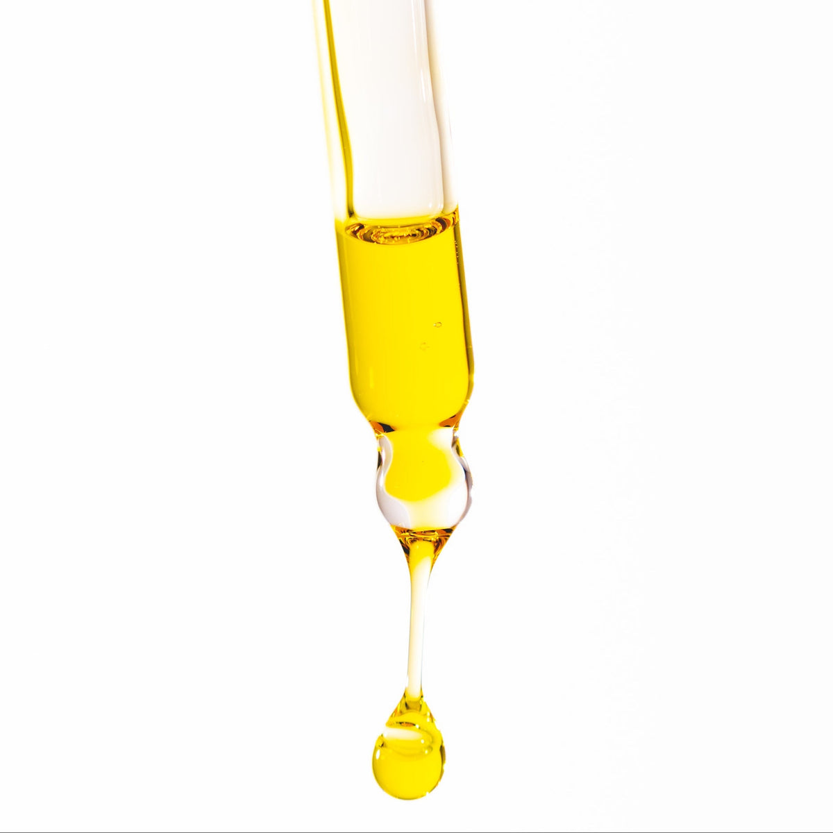 Yellow liquid being dripped from a pipette onto a white background