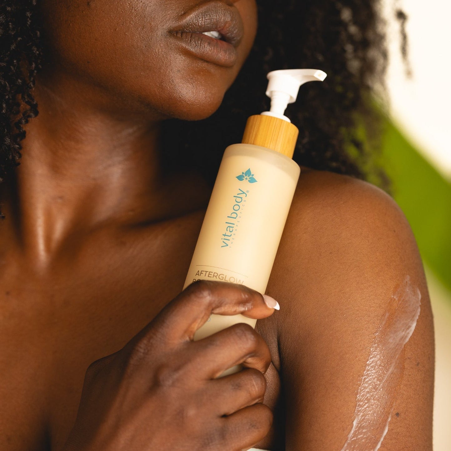 Person applying 'vital body' lotion to their arm with a blurred natural background