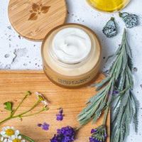 Jar of cream on a wooden board with herbs and flowers