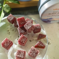 Red gummy bears on a white plate with a container labeled 'Vita' in the background.