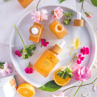 Orange-colored skincare products with flowers and oranges on a white plate