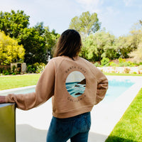 Person wearing a brown sweatshirt with a graphic design, standing by a pool with greenery in the background